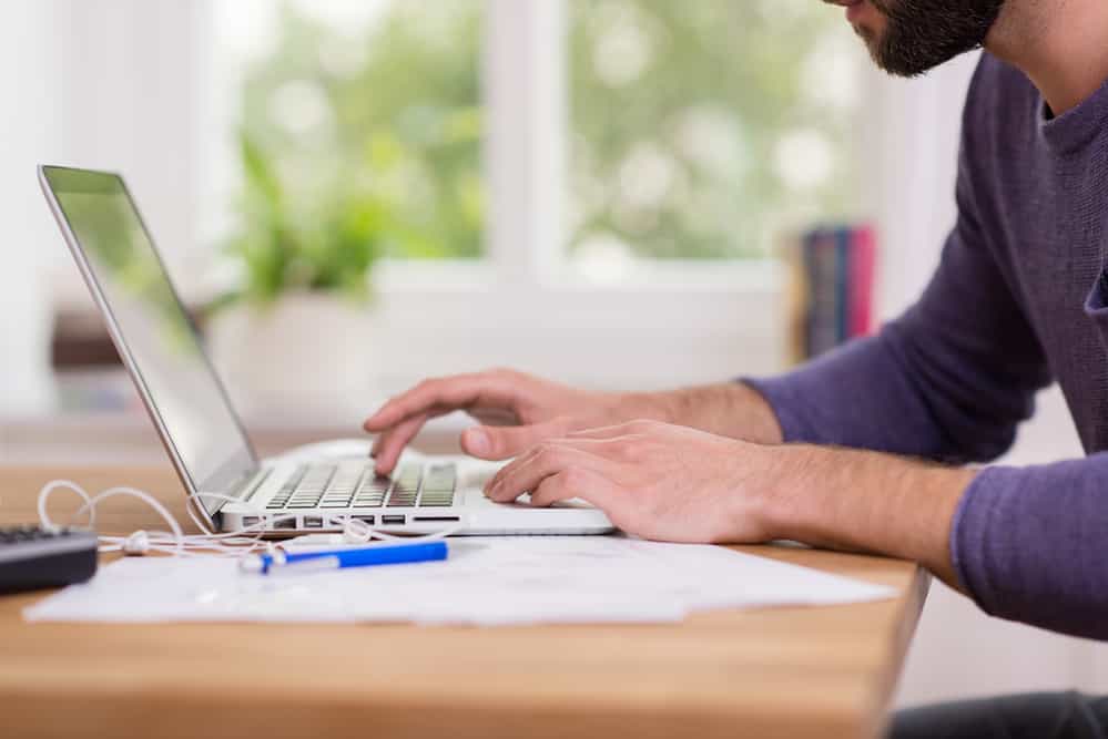 Close up low angle view of a man working from home on a laptop computer sitting at a desk surfing the internet Close up low angle view of a man working from home on a laptop computer sitting at a desk surfing the internet
